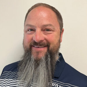 Headshot of a middle-aged man with a long, graying beard, smiling at the camera.