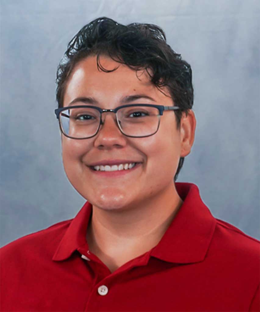 Person with short dark hair, glasses, and a red collared shirt smiling in front of a plain light gray background.