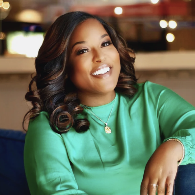 A smiling woman wearing a green long-sleeved blouse and a gold pendant necklace.