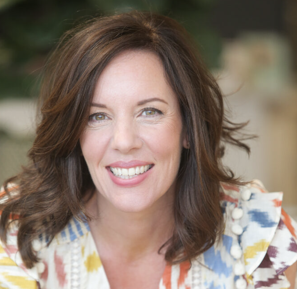 A smiling woman with shoulder-length brown hair wearing a patterned top.